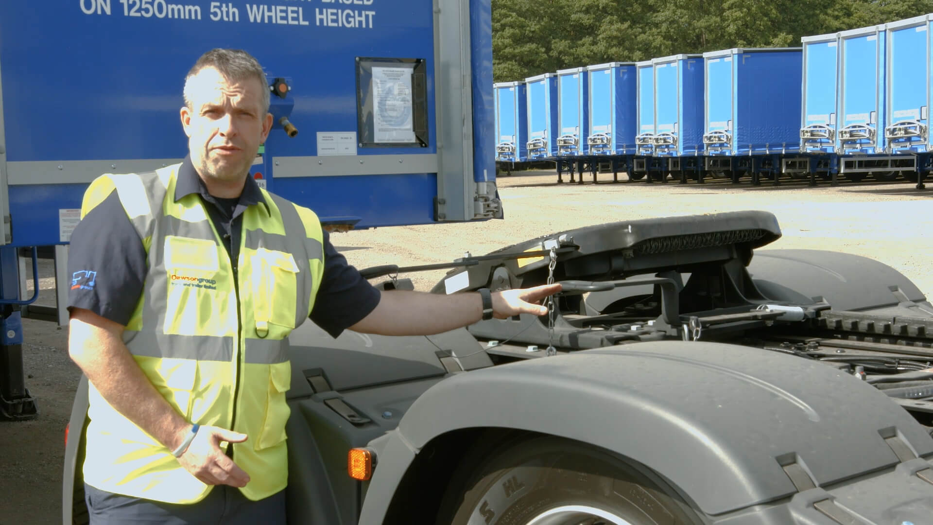 Truck driver in a hi-viz jacket standing next to the back of a tractor unit