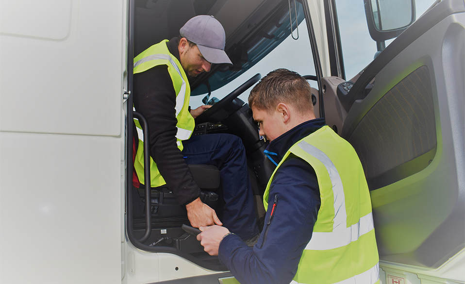 Two men in hi-viz jackets; one sitting in a truck cab and the other standing inside the open door